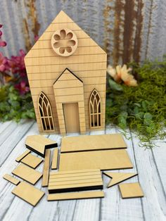 a small wooden church with cut out pieces next to it and flowers in the background