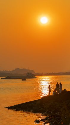 people are standing on the shore watching the sun go down