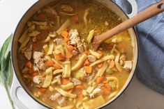 a pot filled with chicken noodle soup on top of a table next to a wooden spoon