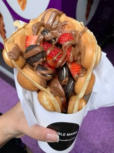 a person holding a waffle filled with chocolate covered strawberries and other toppings