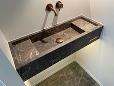 a bathroom sink with two faucets mounted on the wall and marble counter top