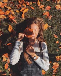 a woman standing in the grass with her hands on her face and looking up at leaves