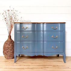 a blue dresser sitting on top of a wooden floor next to a vase with flowers