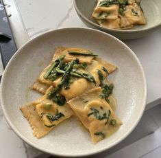 two bowls filled with ravioli and spinach on top of a white countertop