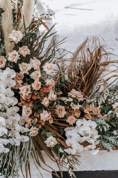 an arrangement of flowers and plants on a table in the snow with dried grass around them