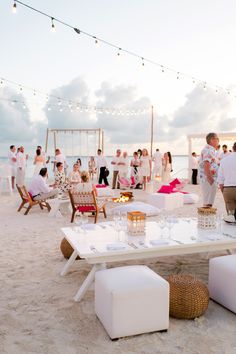 a group of people standing on top of a beach next to a white table and chairs