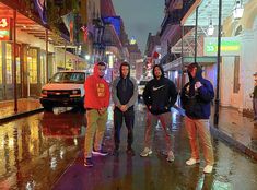 four people standing in the rain on a city street at night with their arms around each other