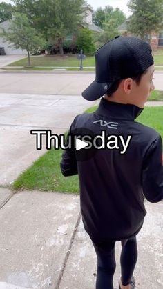 a young boy is walking down the sidewalk wearing a baseball cap and leggings