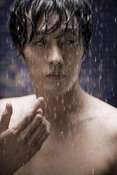 a shirtless man standing in the rain with his hands clasped up to his chest