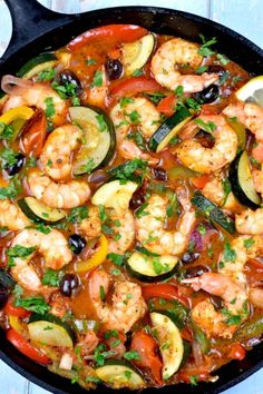 a skillet filled with shrimp, zucchini and olives