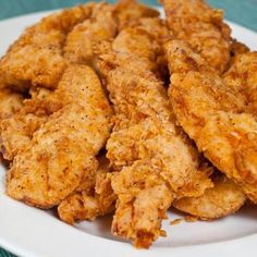 fried chicken pieces on a white plate sitting on a blue tablecloth with a fork