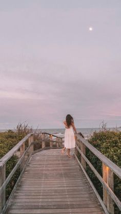 a woman walking across a wooden bridge towards the ocean