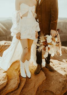 a man and woman standing next to each other on top of a rocky mountain together