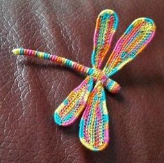 a crocheted dragonfly sitting on top of a leather surface