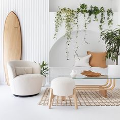 a living room with white walls and plants hanging from the ceiling, along with a surfboard on the wall