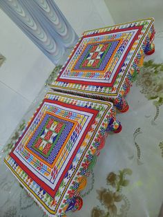 two decorative trays sitting on top of a table covered in colorful fabric and beads