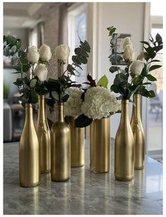 four gold vases with white flowers and greenery in them on a marble countertop