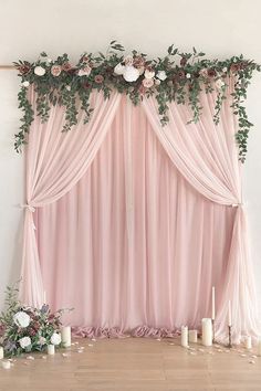 a pink backdrop with roses and greenery on the top, along with candles in front of it