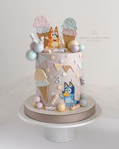 a birthday cake decorated with ice cream and cartoon characters is on a white pedestal in front of a plain background