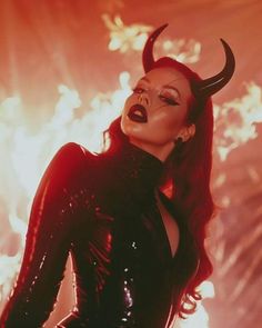 a woman with horns on her head and black catsuits is standing in front of fireworks