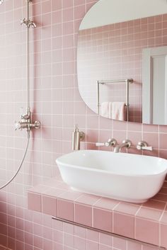 a bathroom with pink tiles and a white sink under a mirror on the wall next to a shower head