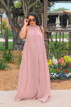 a woman in a pink dress is standing on the sidewalk and talking on her cell phone