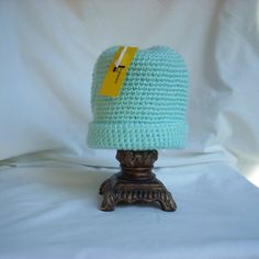 a crocheted blue hat sitting on top of a wooden stand next to a white sheet