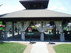 an outdoor gazebo with curtains and tables on the side walk in front of it