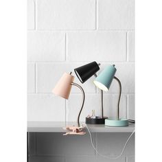 three lamps on a table next to a white brick wall, one is pink and the other is blue