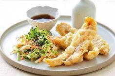 a white plate topped with fried food next to a bowl of sauce and a bottle