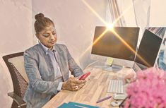 a woman sitting at a desk looking at her cell phone