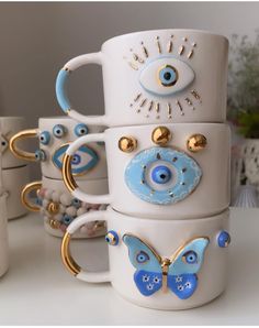 a stack of coffee mugs with eyeballs and gold rings on the handles, all decorated in different colors