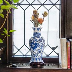 a blue and white vase with flowers in it sitting on a window sill next to books