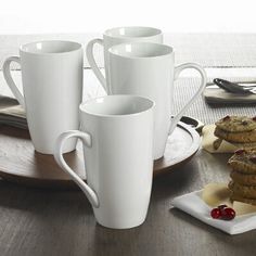 there are four cups and two plates with cookies on the table next to each other