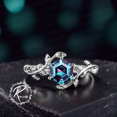 an intricately designed ring sits on top of a black box with a blue stone in the center