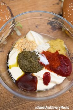 a glass bowl filled with different types of food on top of a wooden table next to buns