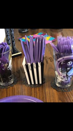 purple and white toothbrushes sitting in plastic cups on a wooden table with other items