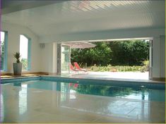 an indoor swimming pool with lounge chairs and umbrella in the middle of it, surrounded by large windows