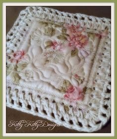 a white crocheted square with pink flowers and leaves on the center is sitting on a table