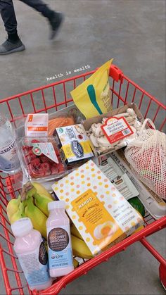 a red shopping cart filled with groceries and condiments on the ground next to a person