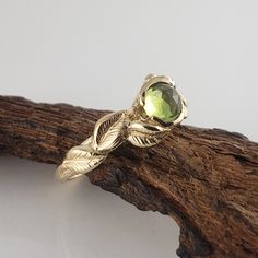 a gold ring with a green stone in the center on top of a piece of wood