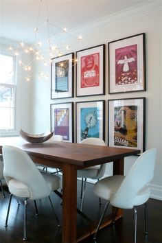 a dining room table with chairs and pictures on the wall above it, along with hanging lights