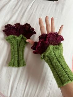 a person's hand wearing green knitted gloves with purple flowers on them, resting on a bed