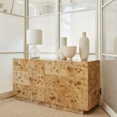 two white vases sitting on top of a wooden cabinet in front of a window