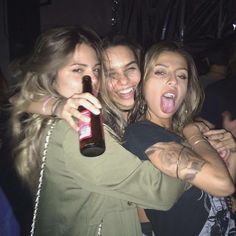 three young women are hugging and having fun at a party, one is holding a beer bottle