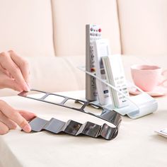 two hands are pulling apart the remote control holder from the table top, while another hand is holding it with their fingers