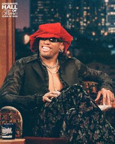 a man wearing a red hat and sunglasses sitting in a chair on the tonight show