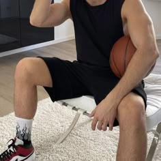 a man sitting on a chair with a basketball in his hand while holding a cell phone to his ear