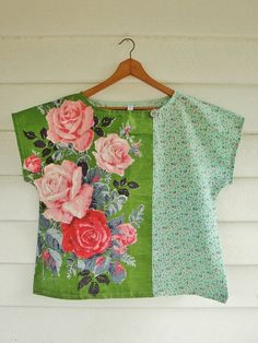 a green top with pink roses on it hanging from a wooden hanger next to a white wall