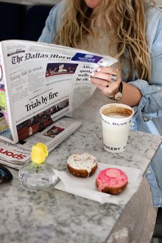 a woman sitting at a table reading a newspaper and holding a cup of coffee in front of her